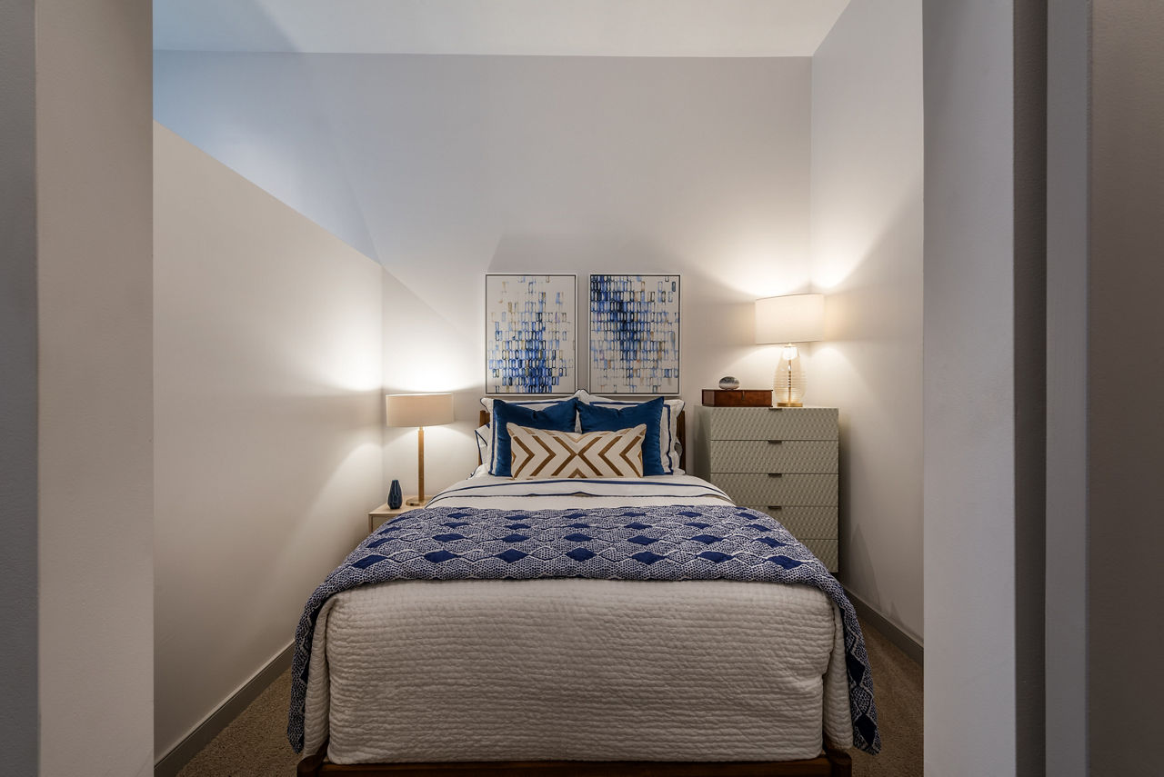 Cozy bedroom featuring a stylish bed, two lamps, dresser, and artwork in luxury apartment