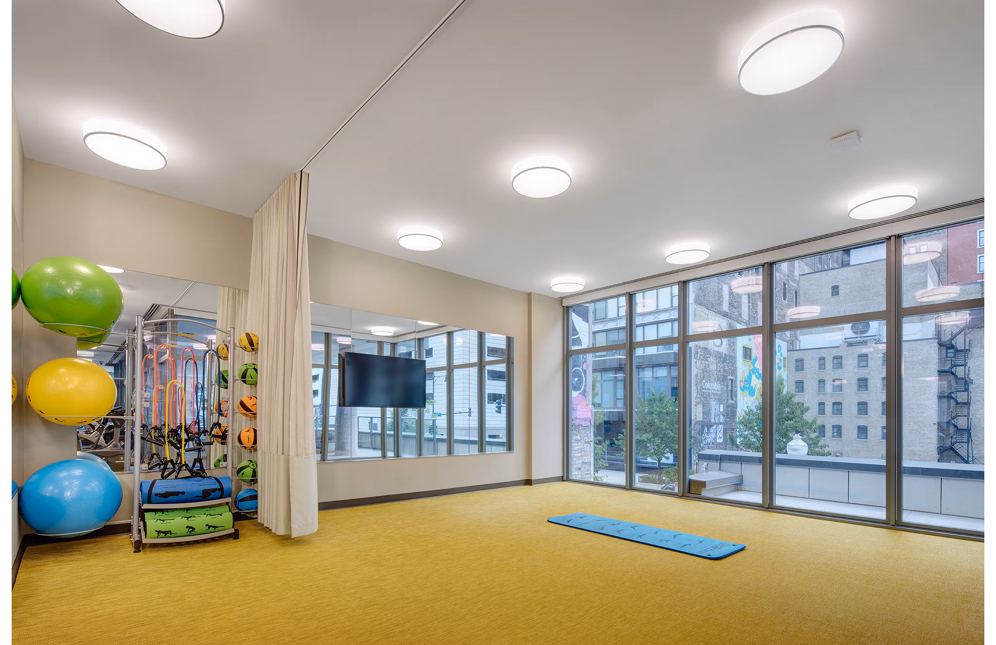 Fitness room featuring exercise balls, resistance bands, and a mat with large windows at luxury apartments
