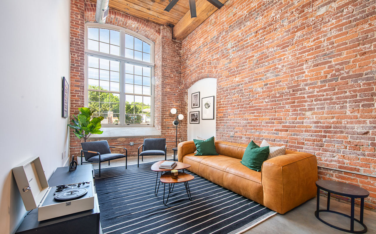 Spacious open-plan living room with exposed brick wall and modern furnishings in The Lofts at Woodside Mill Apartments