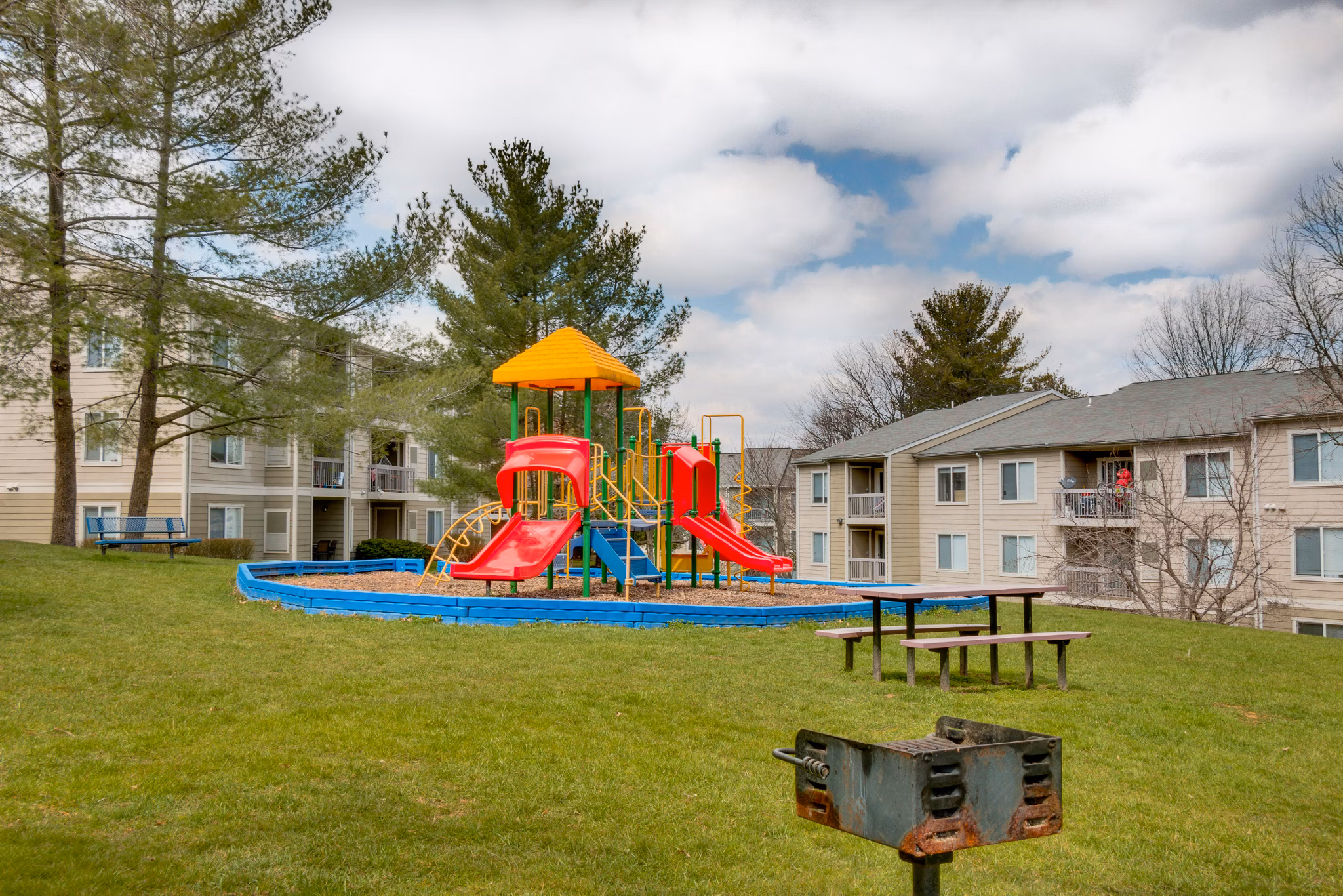 Colorful playground at Avana Oak Mill Apartments featuring slides and swings amid lush greenery