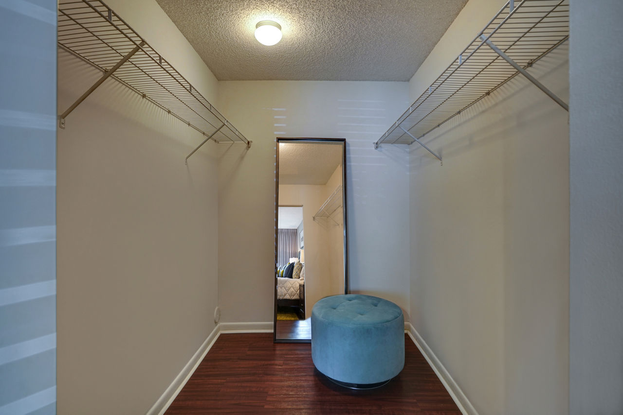 Walk-in closet with mirror, built-in shelves, and blue ottoman in The Plantation Colony Apartments' luxury apartment suites