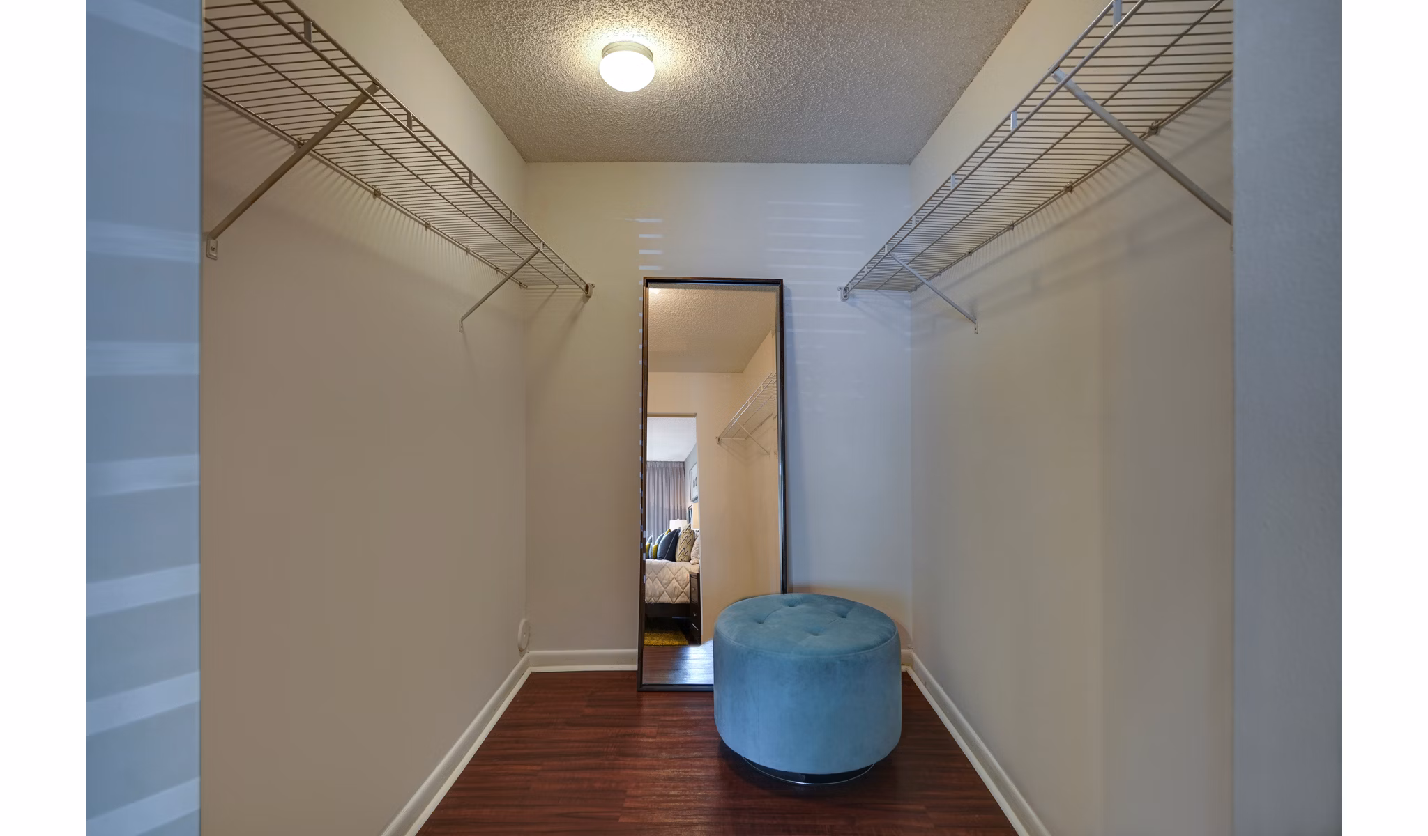Walk-in closet with mirror, built-in shelves, and blue ottoman in The Plantation Colony Apartments' luxury apartment suites