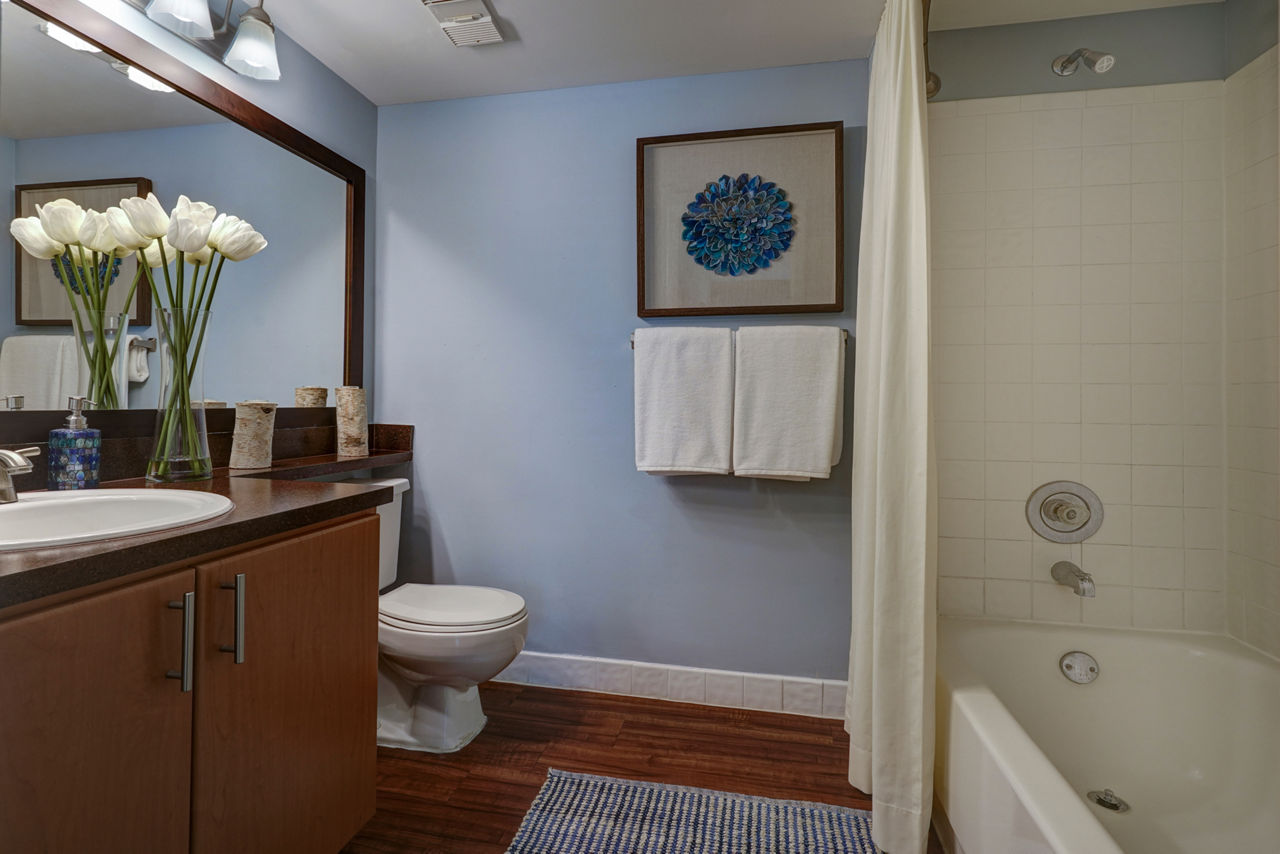 Bathroom with wooden cabinets, white bathtub, and decorative flowers in The Plantation Colony Apartments' luxury space