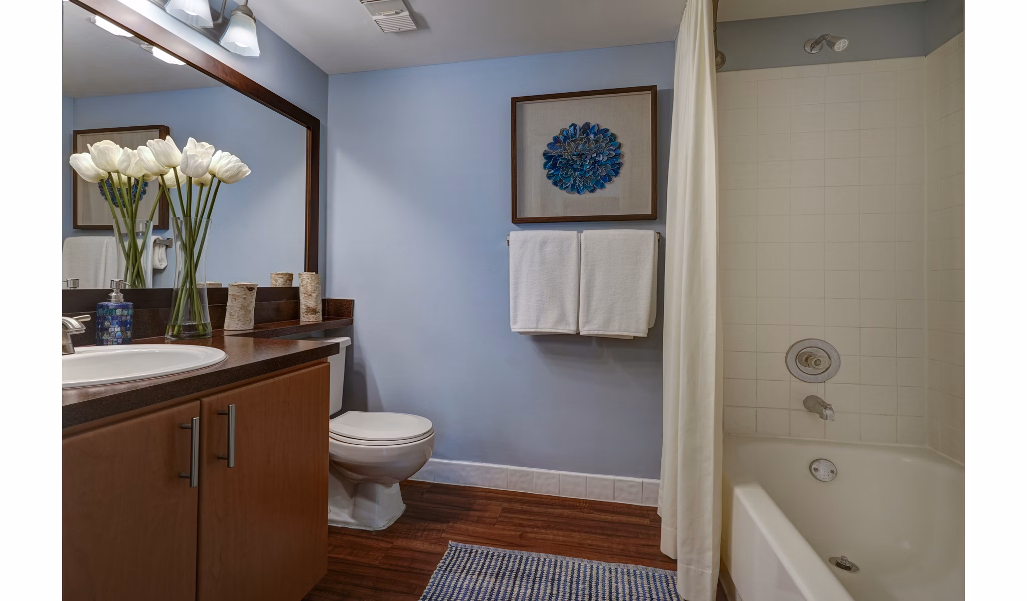 Bathroom with wooden cabinets, white bathtub, and decorative flowers in The Plantation Colony Apartments' luxury space