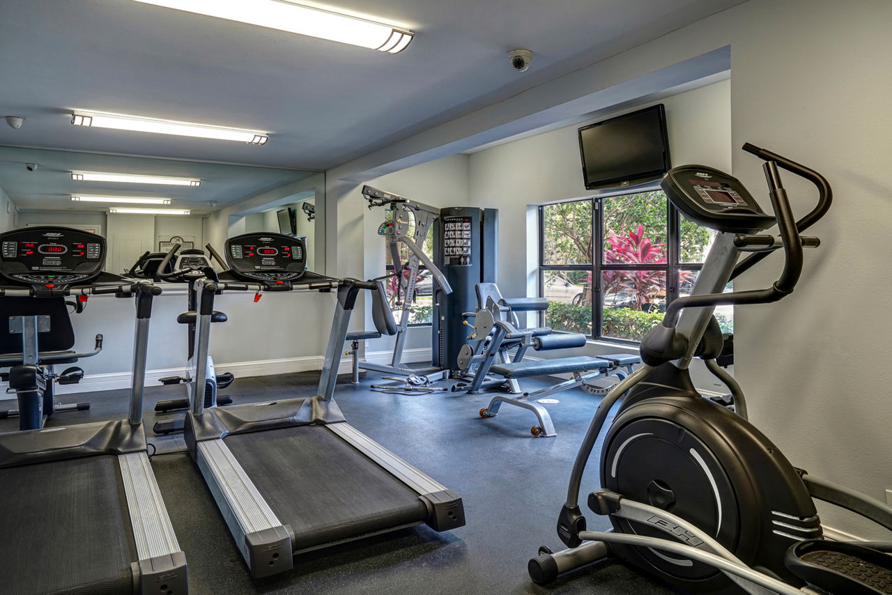Fully-equipped small gym with treadmills, ellipticals, and weight machines at The Plantation Colony Apartments