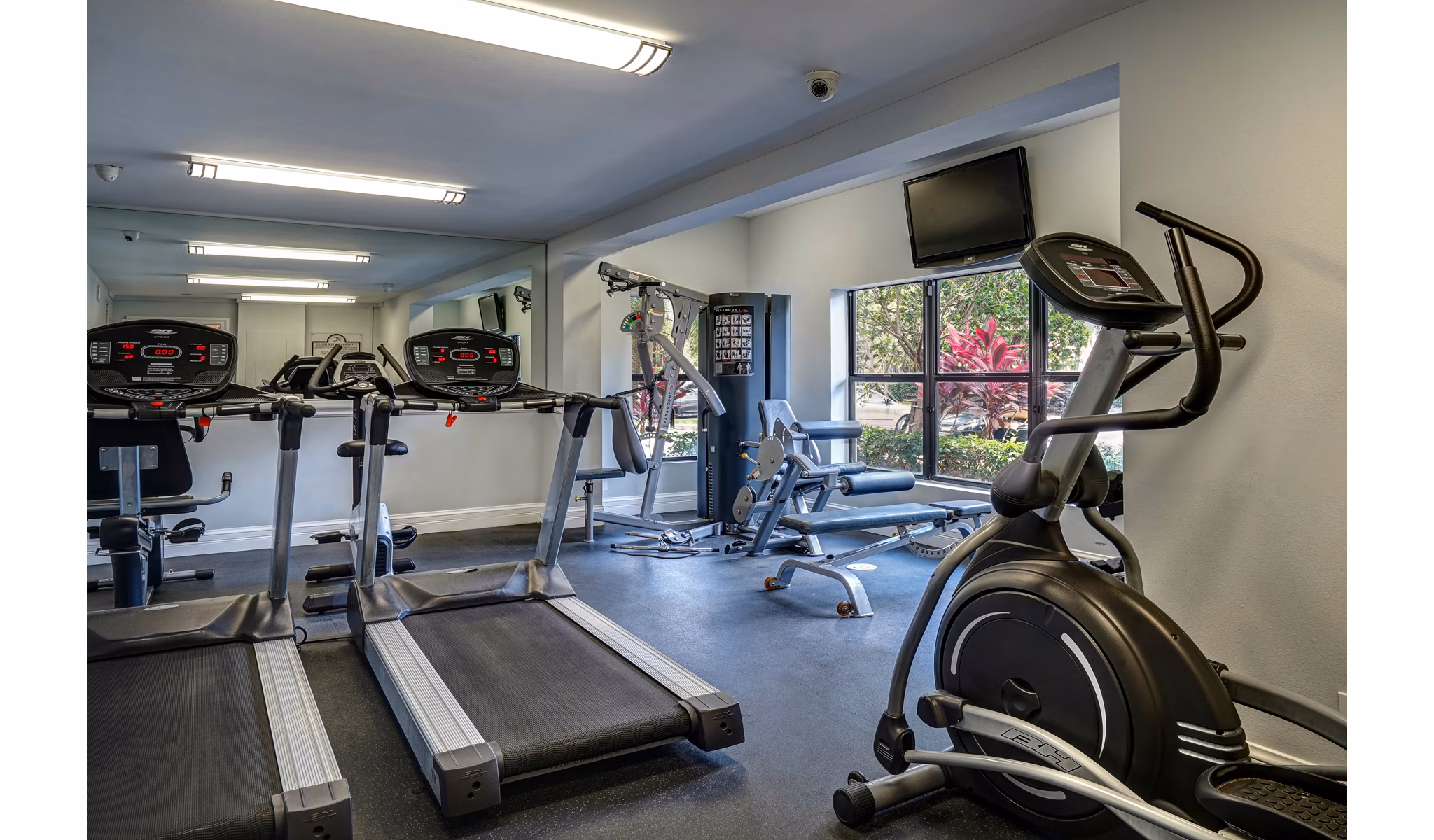 Fully-equipped small gym with treadmills, ellipticals, and weight machines at The Plantation Colony Apartments
