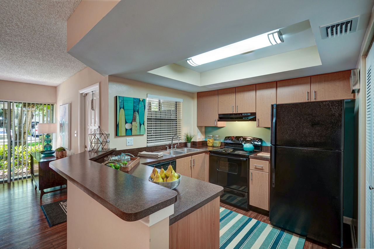 Spacious kitchen with black appliances and wooden cabinets in The Plantation Colony Apartments with a striped rug