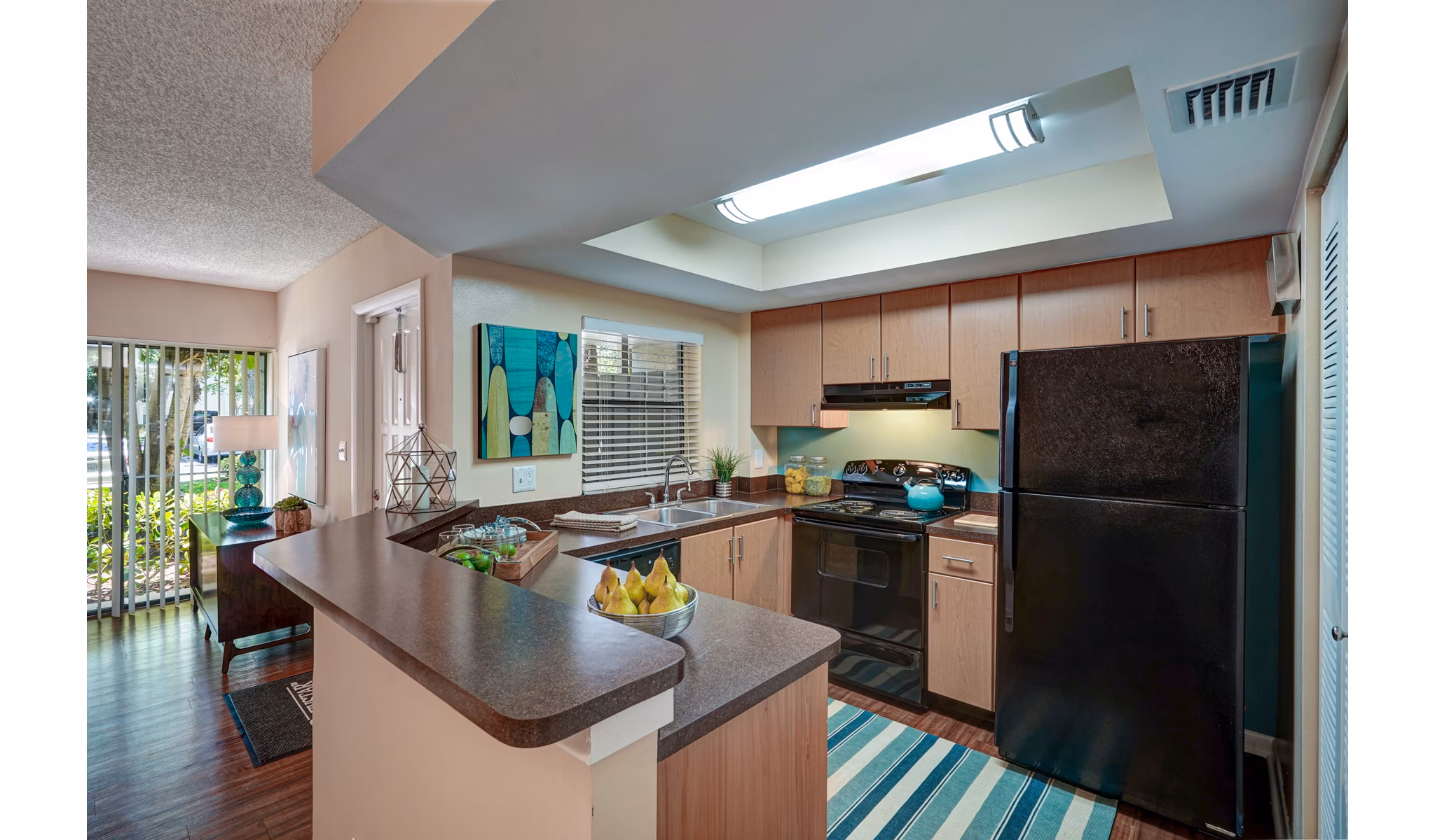Spacious kitchen with black appliances and wooden cabinets in The Plantation Colony Apartments with a striped rug