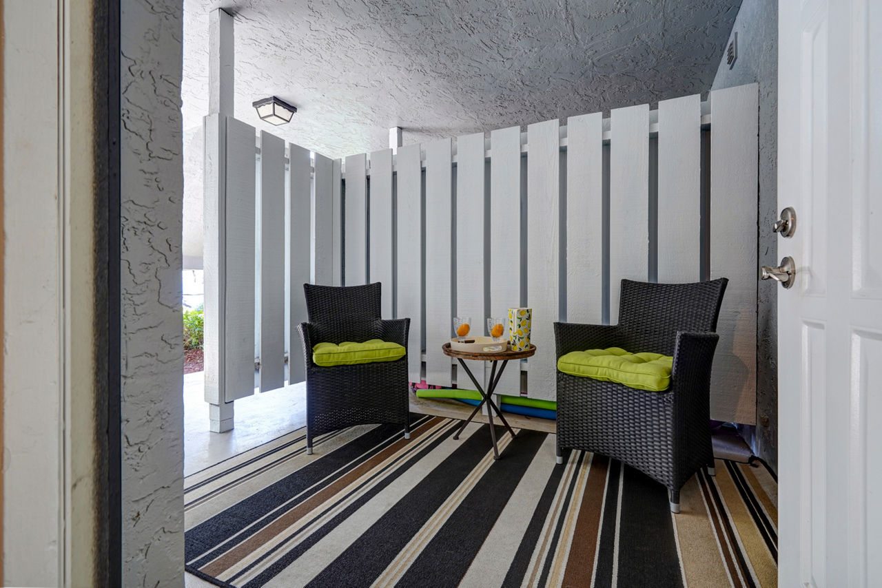 Charming outdoor seating with wicker chairs and green cushions on striped rug at The Plantation Colony Apartments