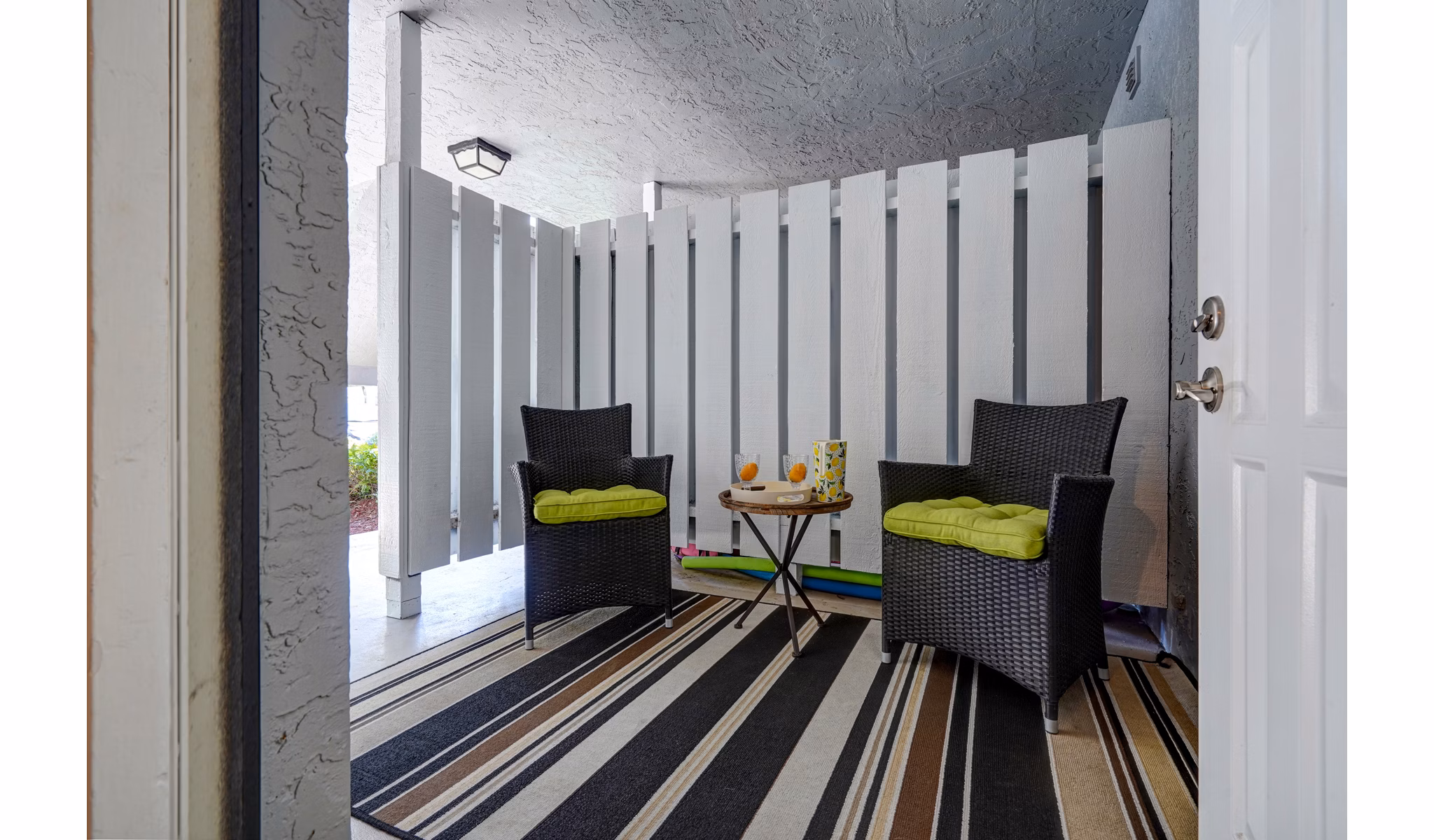Charming outdoor seating with wicker chairs and green cushions on striped rug at The Plantation Colony Apartments
