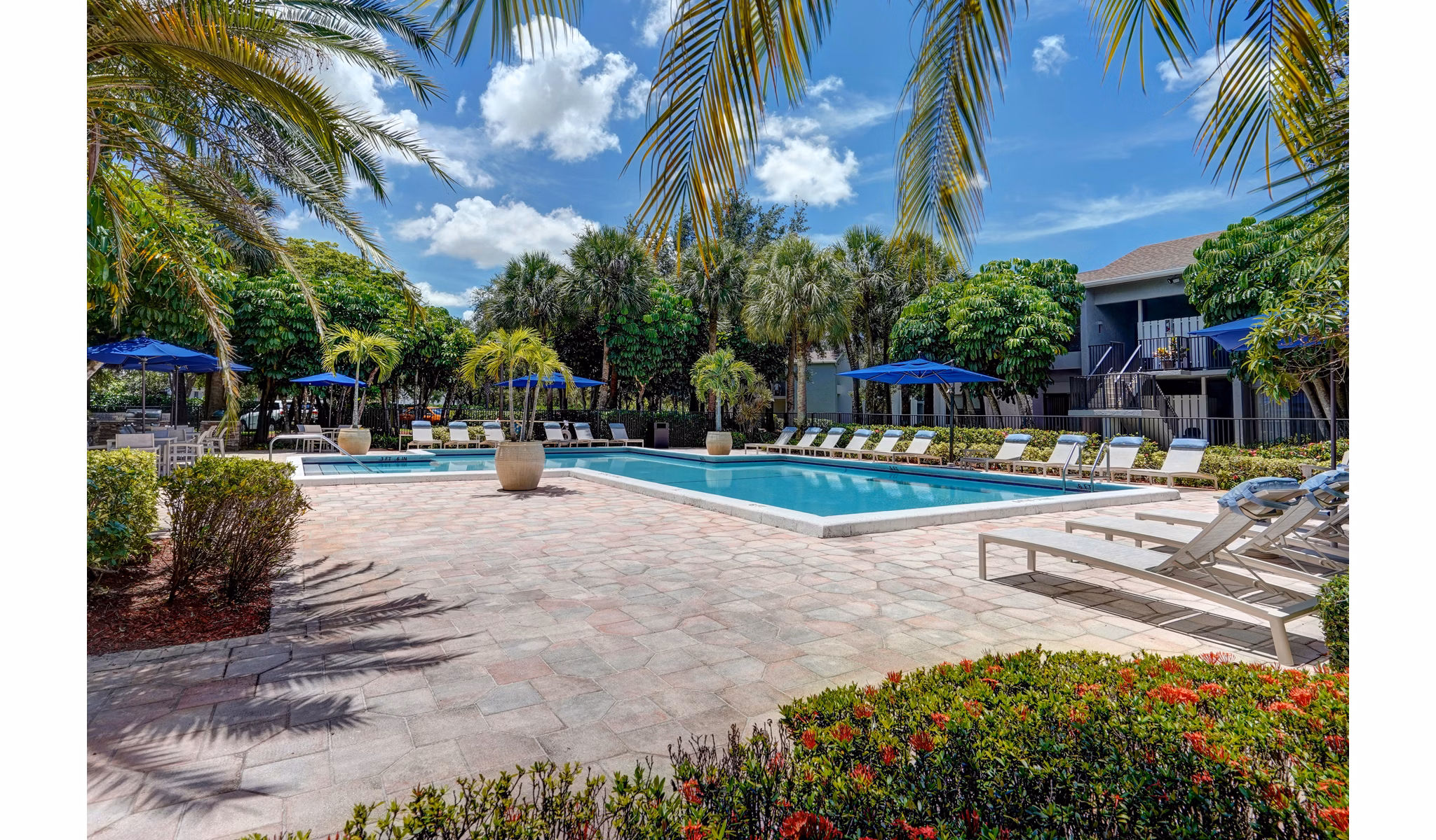 Outdoor pool area with lounge chairs and palm trees at The Plantation Colony Apartments