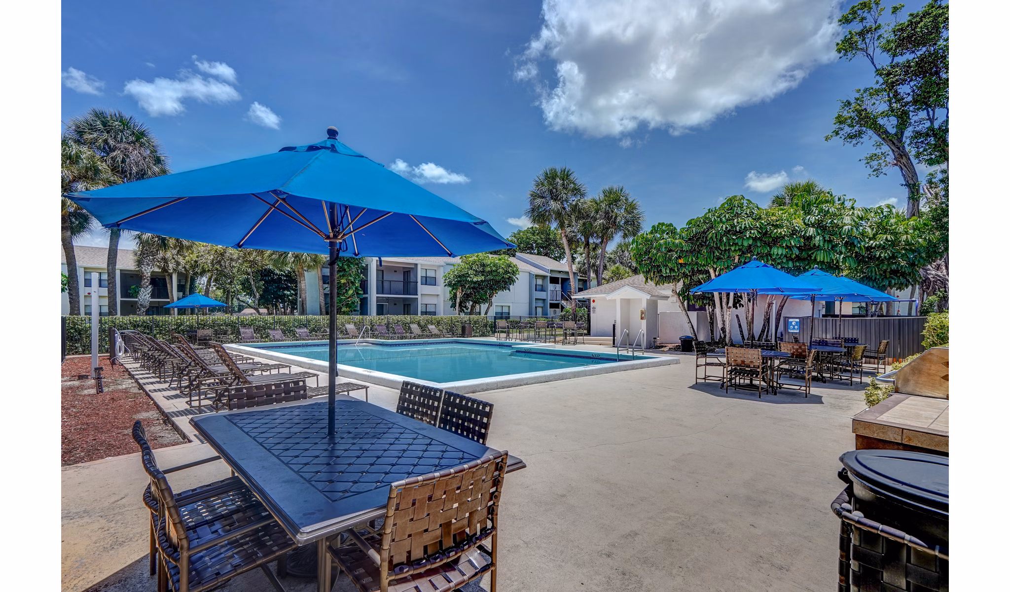 Outdoor pool area with blue umbrellas and patio furniture at The Plantation Colony Apartments
