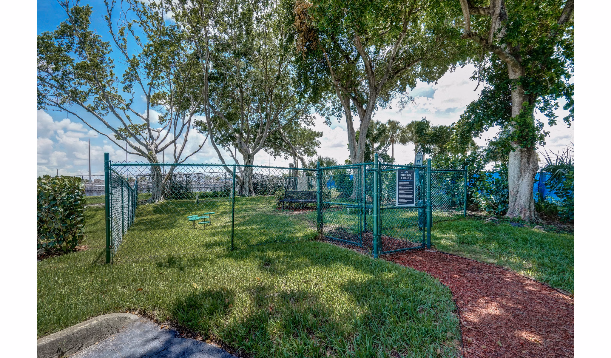 Fenced dog park with trees and a bench at The Plantation Colony Apartments
