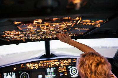 A trainee pilot operating various switches in a flight simulator cockpit