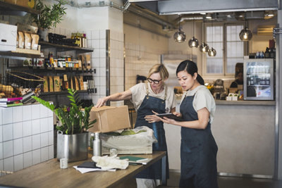 Two women inspect boxes in a retail store while consulting an iPad